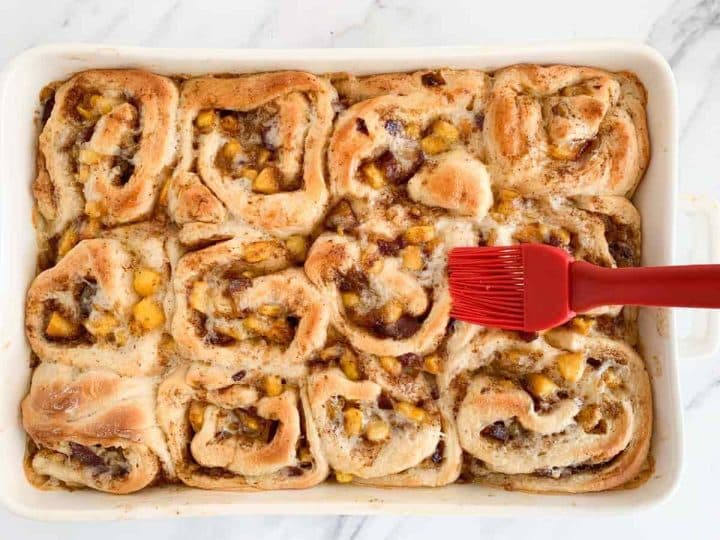 Brushing baked peach cinnamon rolls with melted butter.