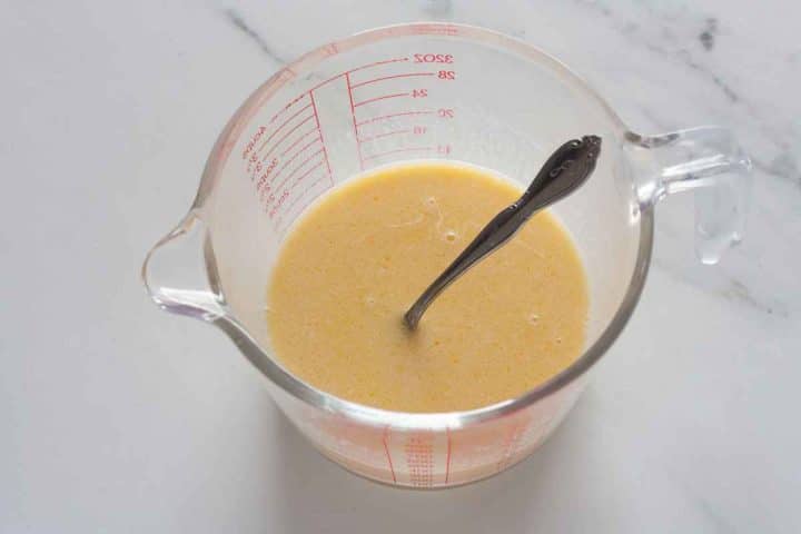 Stirring a beaten egg into milk and melted butter in a glass measuring cup.