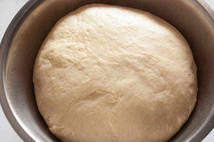 Risen dough in a metal bowl for cinnamon rolls.