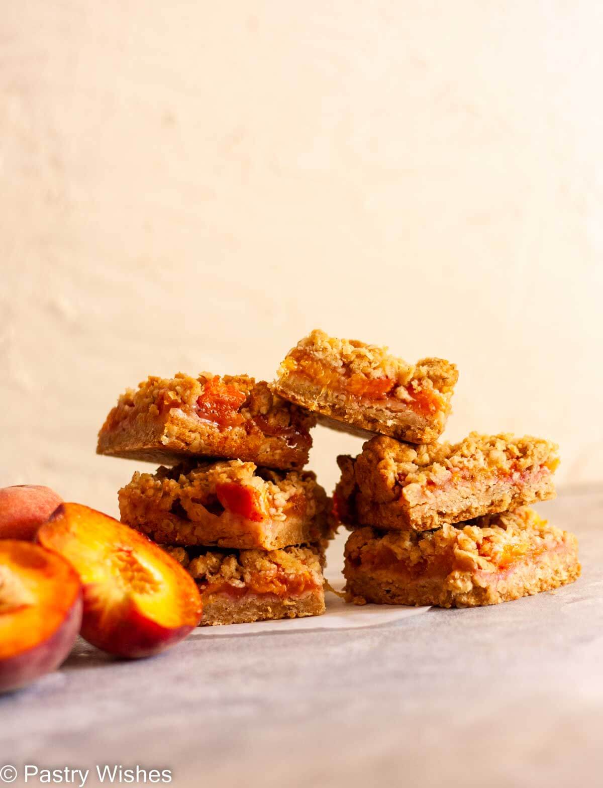 Two stacks of peach crumble bars next to sliced peaches.