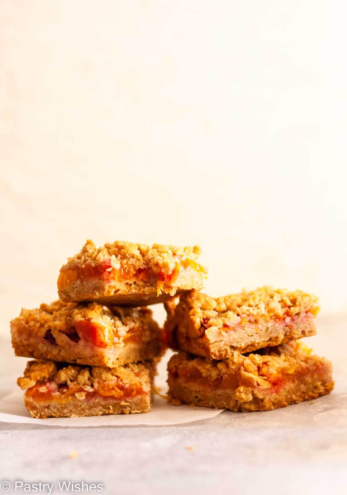 Two stacks of peach crumble bars on parchment paper.