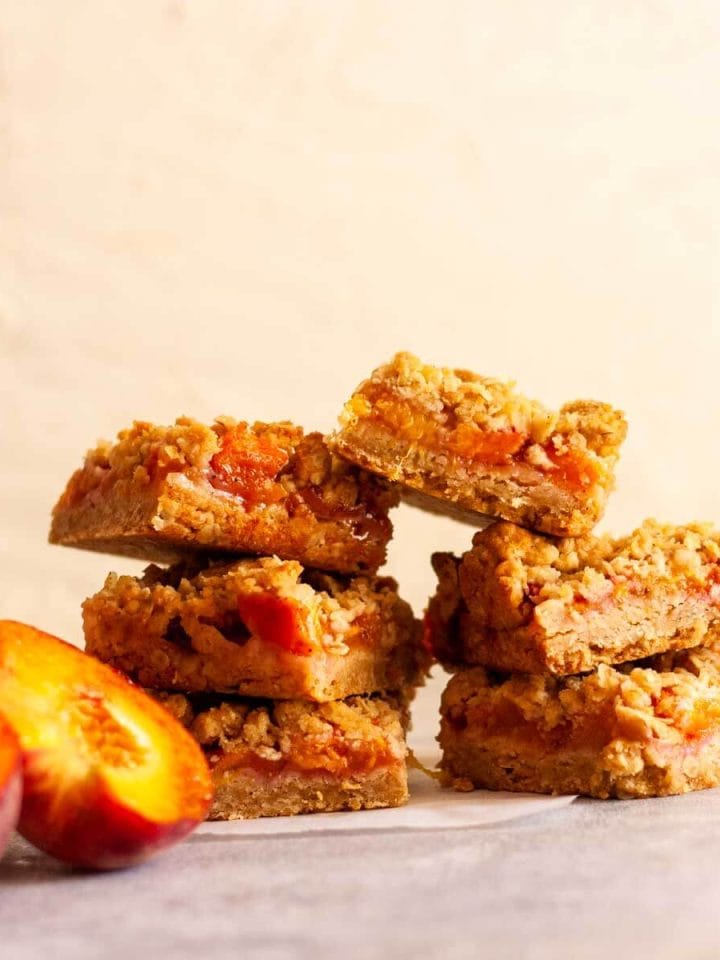 A close of of two stacks of peach crumble bars next to sliced peaches.
