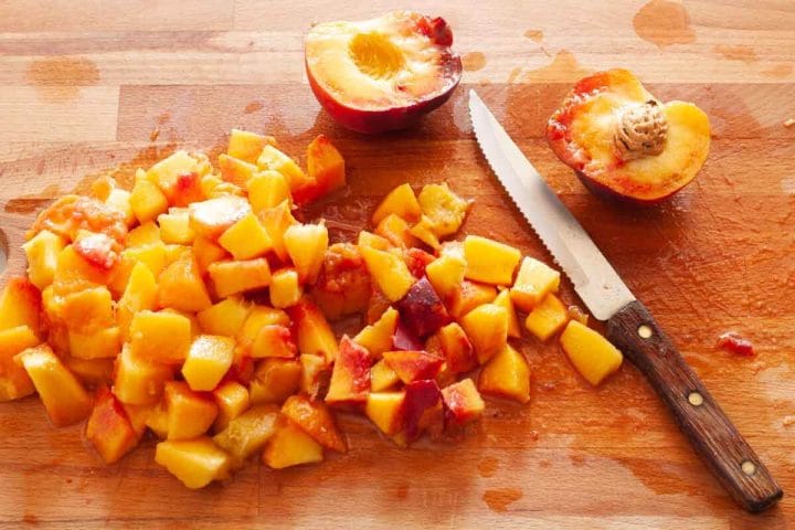 Chopped fresh peaches on a wooden cutting board with a knife.