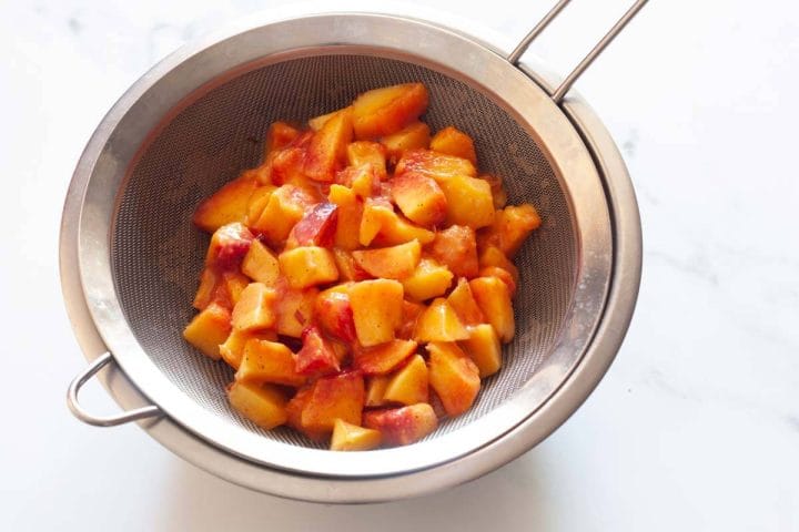 Chopped peaches in a sieve over a metal bowl.