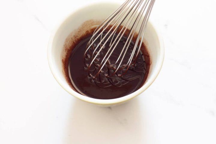 Whisking melted butter, cocoa powder, and vanilla in a glass bowl.