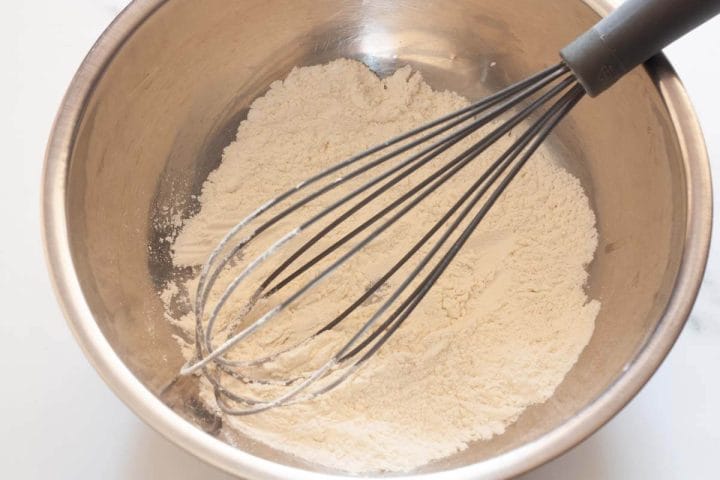 Whisking flour and baking powder in a metal bowl.