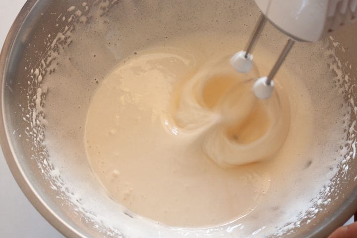 Beating eggs, sugar, and salt with a hand mixer in a metal bowl.