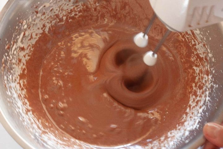 Beating the melted cocoa mixture with the eggs and sugar with a hand mixer.