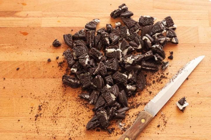 Chopped Oreo cookies on a wooden cutting board with a knife.