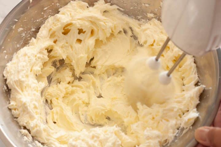 Beating the cream cheese and sugar with a hand mixer in a metal bowl.