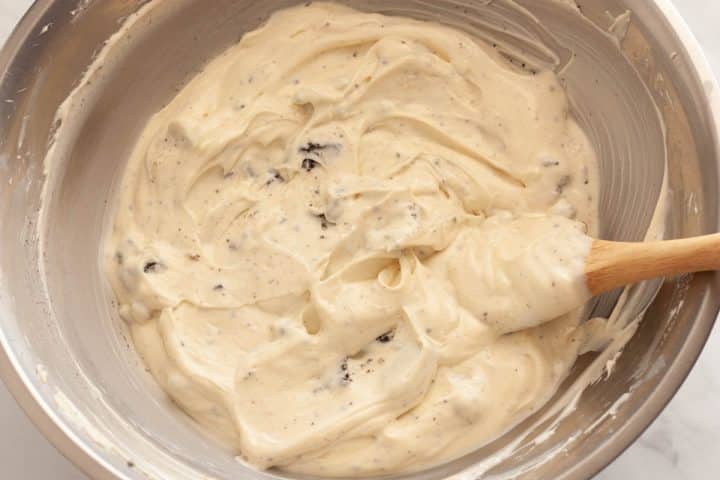 Folding chopped Oreo cookies in cheesecake filling in a metal bowl with a silicone spatula.
