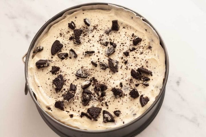 Cheesecake filling over partially baked brownie base, topped with chopped Oreos before being baked.