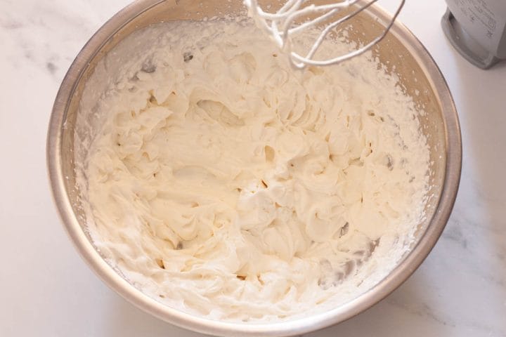 Cream whipped to stiff peaks in a metal bowl.