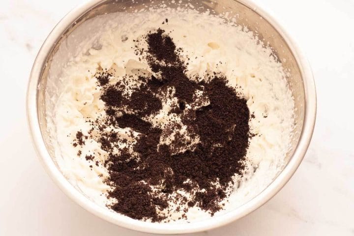 Finely ground Oreo cookies over whipped cream in a metal bowl.
