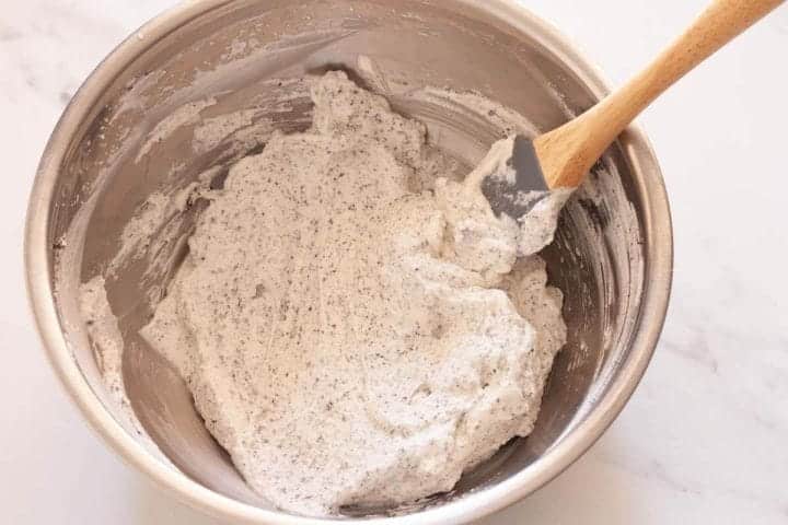 Folding finely ground Oreo cookies with whipped cream in a metal bowl.