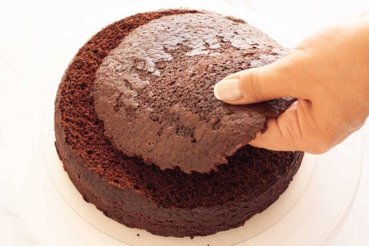 A hand holding a leveled cake top on top of a cake layer.