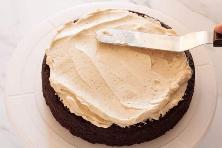Spreading cinnamon buttercream on a spiced chocolate cake layer on a turntable with an offset spatula.