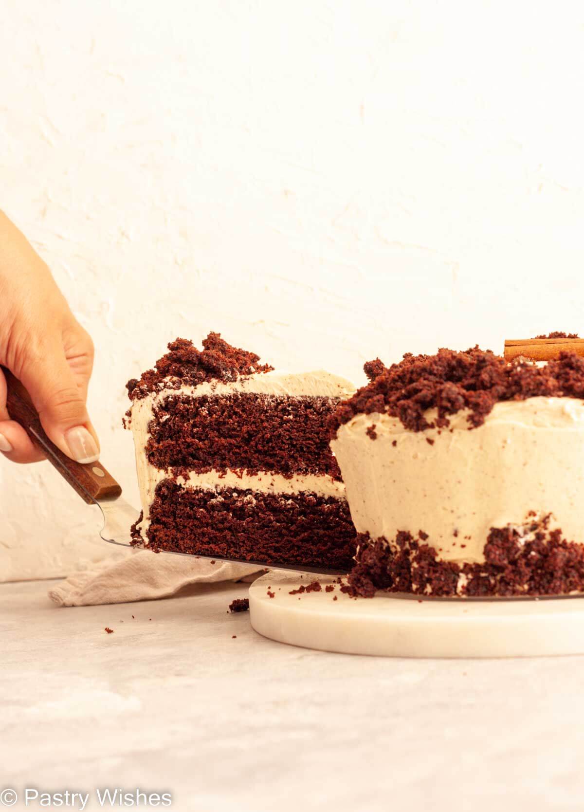 A hand cutting a slice of spiced chocolate cake on a cake server.