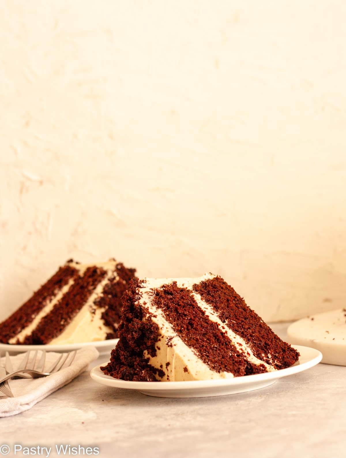 Two plates with a slice of spiced chocolate cake next to a gray towel and forks.