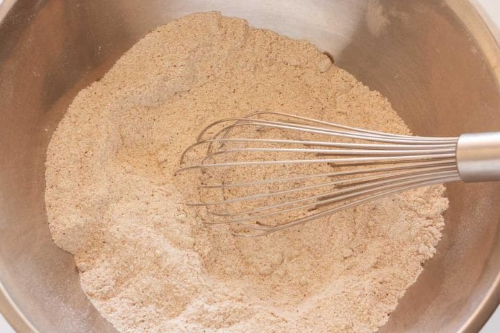 Whisking flour, sugar, baking powder, baking soda, salt, and spices in a large metal mixing bowl.