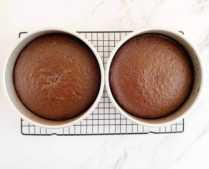 Two round baked spiced chocolate cakes in cake pans on a wire rack.