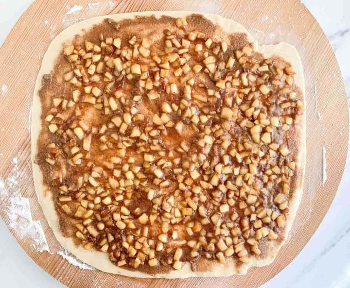 Apple pie filling over rolled out cinnamon roll dough on a wooden board.