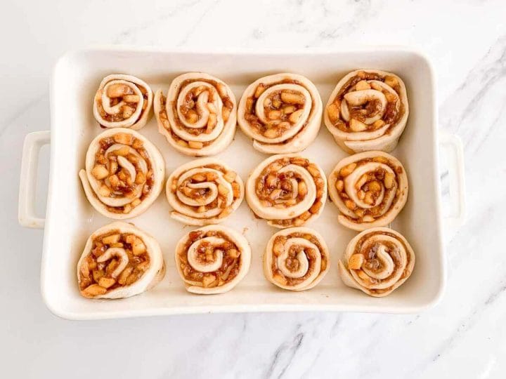 Apple pie cinnamon rolls in a white baking dish before baking.