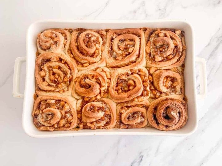 Baked apple pie cinnamon rolls in a white baking dish.