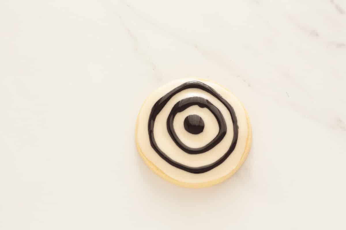 Two black rings around a black dot over white glaze on a sugar cookie.