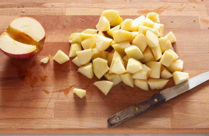 Peeled, cored, and chopped apples on a wooden cutting board next to a knife.