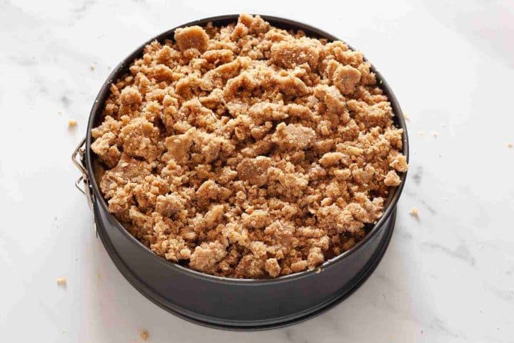 Crumble topping over apple filling in a springform pan before baking.