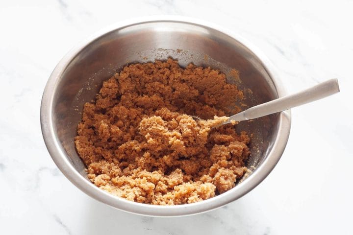 Crushed cookie crumbs and melted butter mixed together in a metal bowl with a spoon.