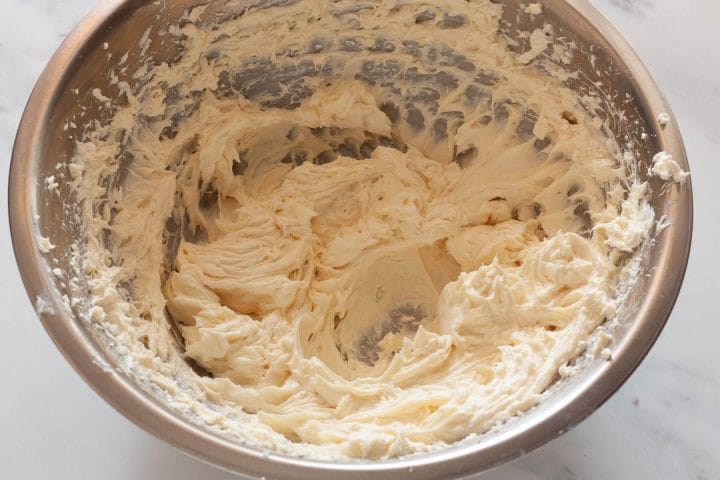 Cream cheese mixed with sugar and vanilla extract in a metal bowl.