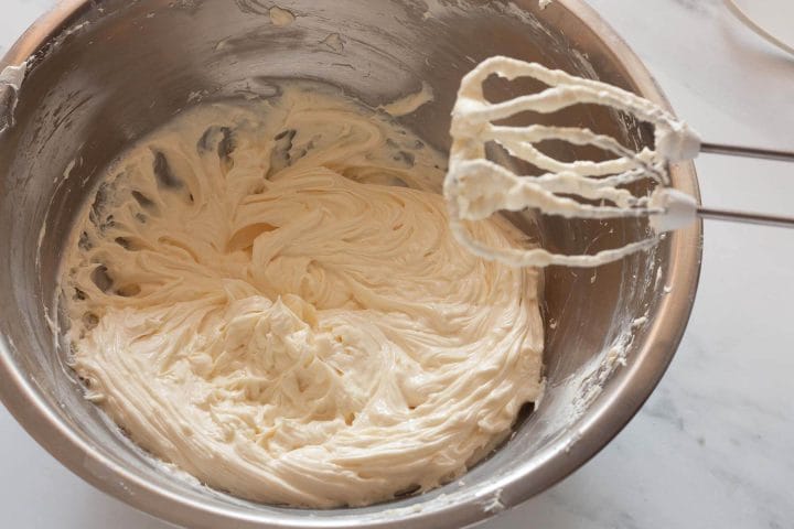 Beating Greek yogurt and lemon juice into cream cheese mixture with a hand mixer.