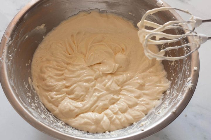 Beating eggs into cream cheese mixture with a hand mixer.