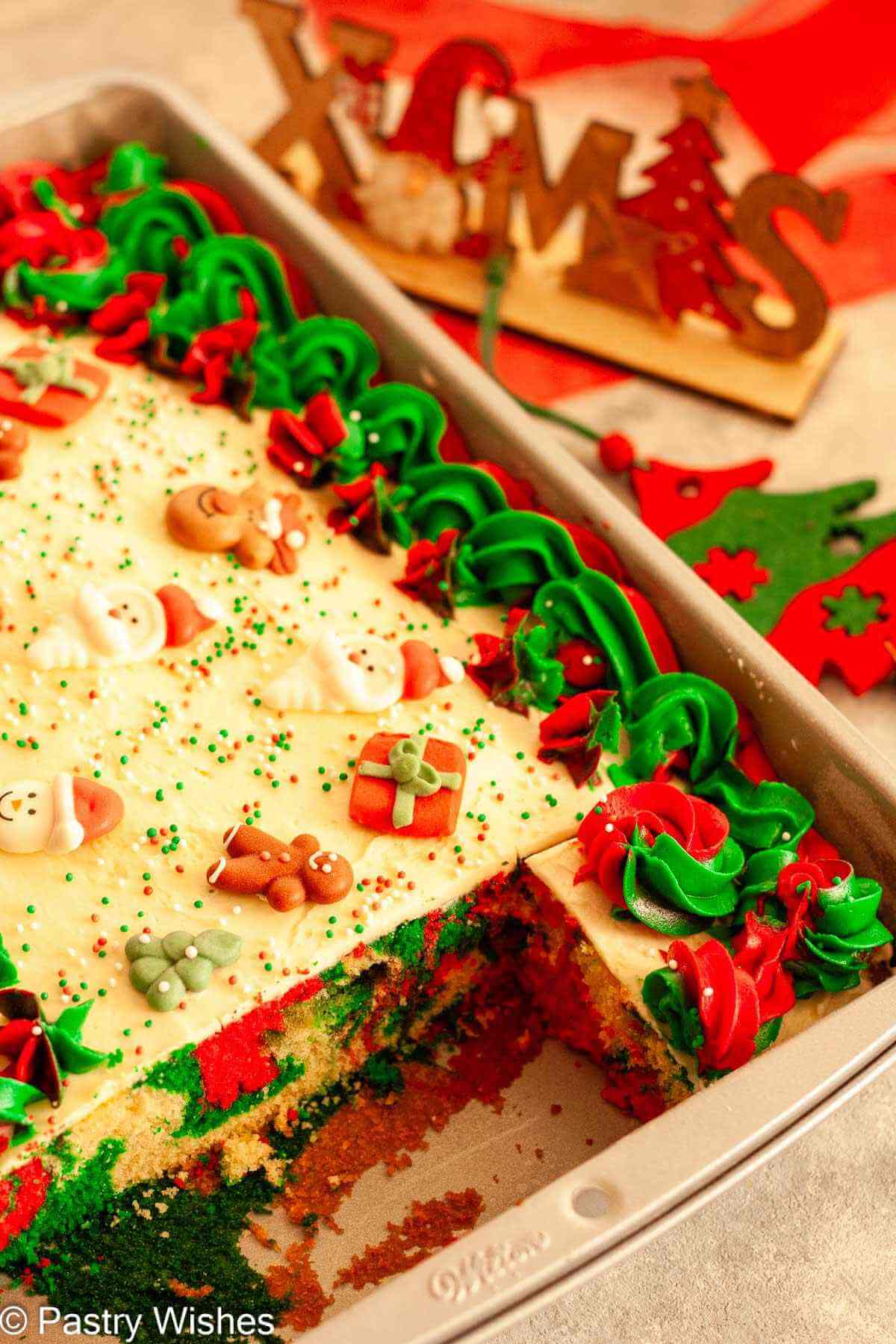 An overhead shot of a sliced, marbled Christmas sheet cake next to Christmas decorations.