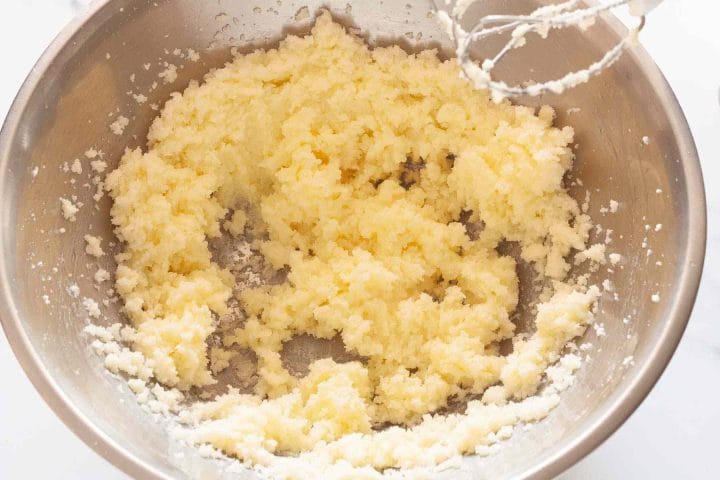 Beating butter and sugar together with a hand mixer in a metal bowl.