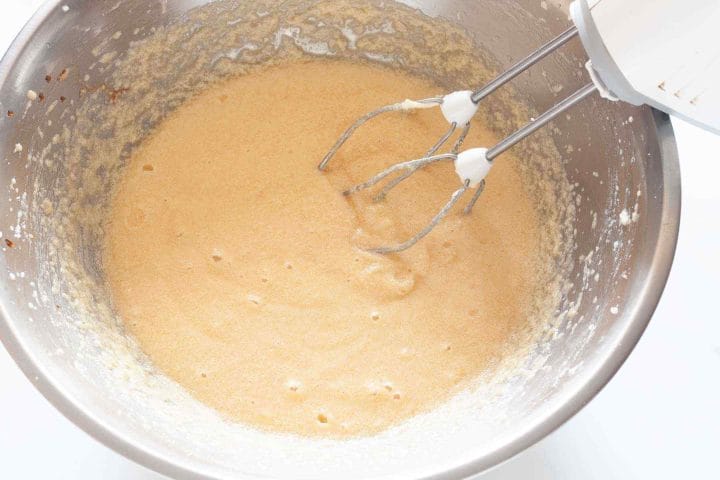 Beating eggs, oil and vanilla into butter and sugar in a metal bowl with a hand mixer.