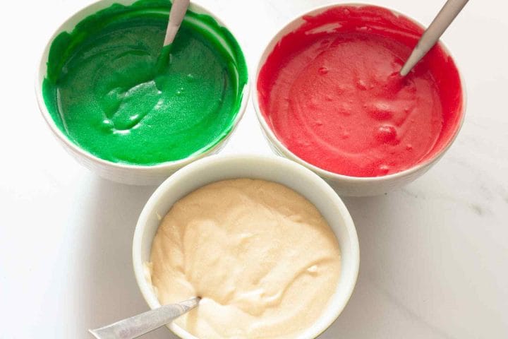 Three bowls of cake batter, two of which are tinted green and red.