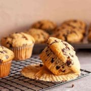 A close up of a dairy-free chocolate chip muffin on its side on top of a muffin liner on a wire rack.