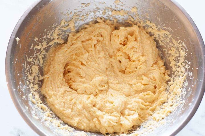 Vanilla extract and eggs mixed with butter and sugar in a metal bowl