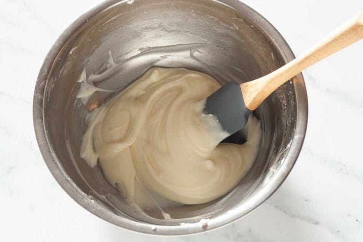 Lemon cream cheese glaze in a bowl with a rubber spatula.