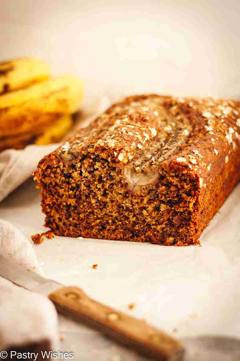 A closeup of dairy-free banana bread on parchment paper, next to ripe bananas and a knife.