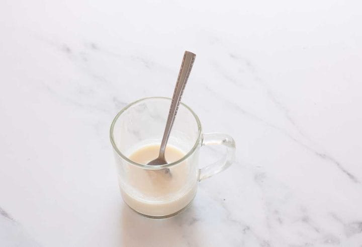 Dairy-free milk and vinegar in a glass cup stirred with a spoon.