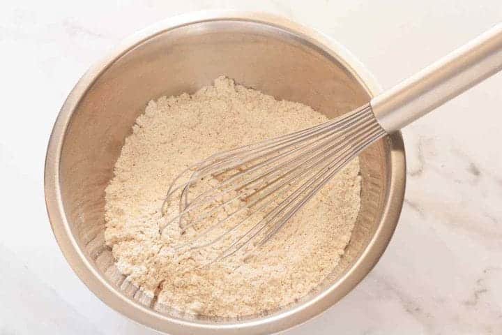Flour, baking powder, baking soda, salt, and cinnamon in a metal bowl with a whisk.