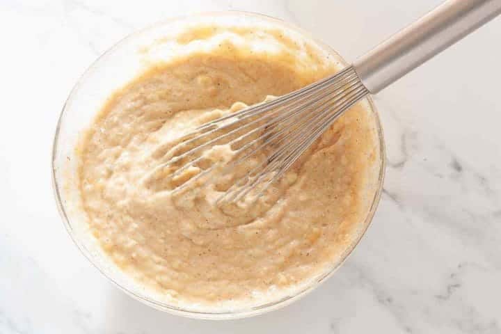 Dairy-free banana bread batter in a glass bowl with a whisk.
