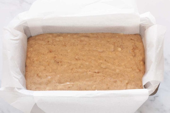 Dairy-free banana bread batter in a lined loaf pan before baking.
