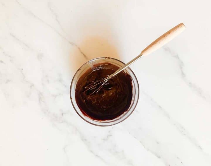 Unsweetened cocoa powder mixed with hot water in a small glass bowl with a whisk.