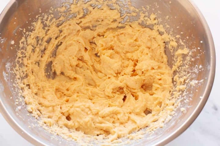 Eggs and vanilla mixed iwth buttter and sugar in a metal bowl.