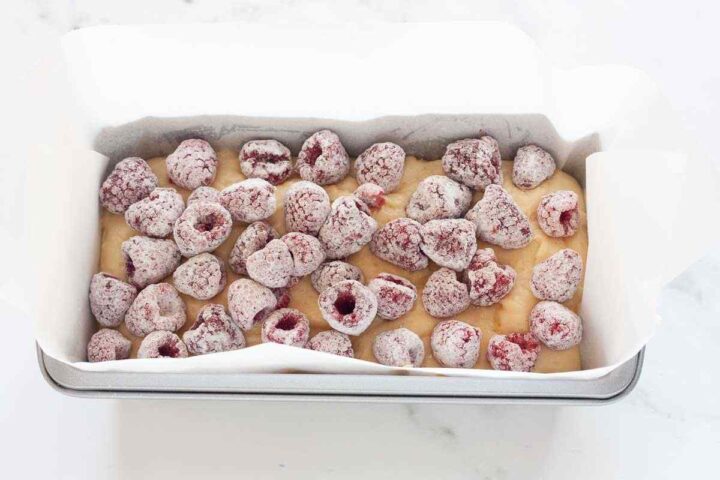 Raspberries layered over batter in lemon raspberry loaf cake.